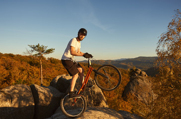 Professional sportsman cyclist standing on back wheel on trial bicycle. Bicyclist looking to the camera, making acrobatic trick on the top of mountain. Concept of extreme sport active lifestyle