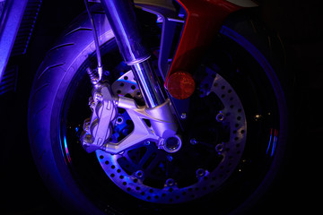 The front wheel of a modern motorcycle with blue lighting. Studio shooting.