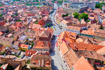 Naklejka premium Aerial view of Sibiu traditional houses with brown-orange roofs and a street in the middle, near the city pedestrian area/center. View from the watch tower of Lutheran Cathedral of Saint Mary.