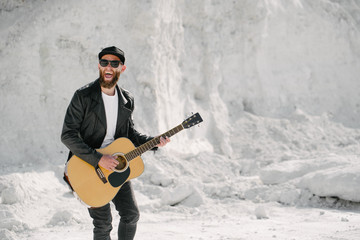 Guitar player singing outside. Hipster guitar player with beard and black clothes