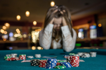 Upset woman in casino sitting behind poker table - obrazy, fototapety, plakaty