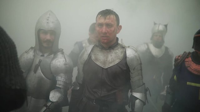 Combat squad of medieval knights of the Crusaders stand in armors and helmets with their swords and shields preparing to attack  against background of smoke in the forest.