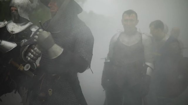 Combat squad of medieval knights of the Crusaders fights with the enemy with swords in misty morning.