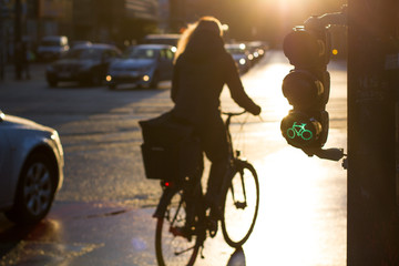 Green bicycle traffic light with woman riding a bicycle across the street during sunrise