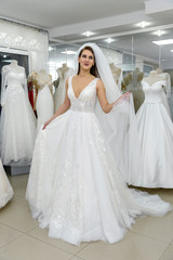 Attractive young bride choosing wedding dress in wedding salon