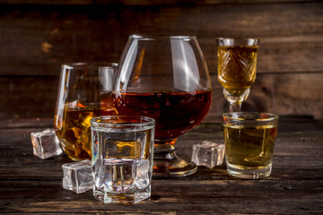 Assortment various hard and strong alcoholic drinks in different glasses: vodka, cognac, tequila, brandy and whiskey, grappa, liqueur, vermouth, tincture, rum, etc. Wooden background copy space
