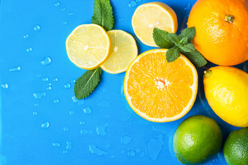 Heap of raw juicy citrus fruits oranges lemons lime fresh mint on wet blue background with water drops. Summer beverages refreshments drinks cocktails ingredients. Healthy diet vitamins concept
