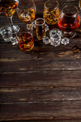 Assortment various hard and strong alcoholic drinks in different glasses: vodka, cognac, tequila, brandy and whiskey, grappa, liqueur, vermouth, tincture, rum, etc. Wooden background copy space
