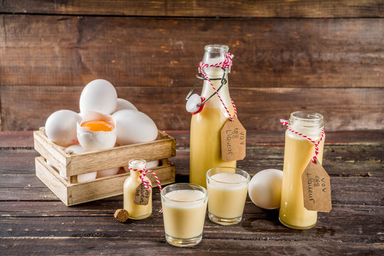 Traditional Italian Vov eggs liquor. German Egg Liqueur Eierlikor. In different bottle and shot glasses, Wooden background copy space