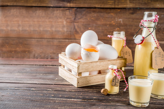 Traditional Italian Vov eggs liquor. German Egg Liqueur Eierlikor. In different bottle and shot glasses, Wooden background copy space