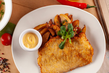 Crispy chicken schnitzel with baked potato and mustard on rustic wooden table
