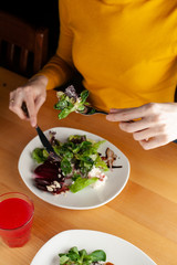 Woman is eating a healthy beetroot salad with greens, almond and cream cheese, served on a wooden rustic table