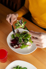 Woman is eating a healthy beetroot salad with greens, almond and cream cheese, served on a wooden rustic table