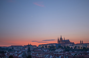 Obraz premium Orange sky sunset behind Prague Castle, with crescent moon in sky