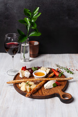 Assorted cheese as a perfect gourmet appetizer to a glass of red wine: bread sticks, bree, gouda, honey, parmesan, camembert and strawberries, served on a wooden board, on a black and white background