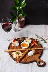 Fototapeta na wymiar Assorted cheese for wine: bread sticks, bree, gouda, honey, parmesan, camembert and strawberries, served on a wooden board, on a black and white background