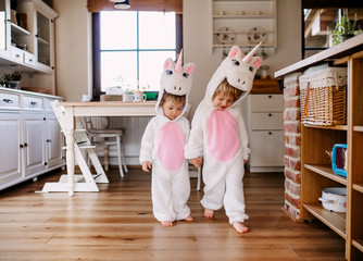 Two toddler children with unicorn masks walking indoors at home.