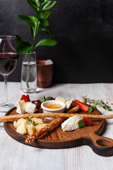 Assorted cheese as a perfect gourmet appetizer to a glass of red wine: bread sticks, bree, gouda, honey, parmesan, camembert and strawberries, served on a wooden board, on a black and white background