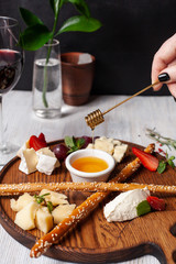 Appetizer to a glass of wine: assorted cheese, strawberries, crunchy bread sticks and pouring sweet flower honey, served on a wooden board on a minimalistic background