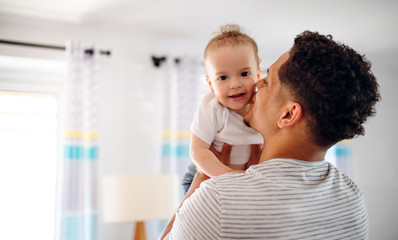 Fototapeta premium A portrait of father and small toddler son indoors at home, kissing.