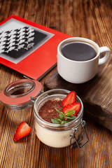 Traditional italian dessert tiramisu with mascarpone and cocoa with black coffee served on a dark wooden table with a book