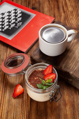 Traditional italian dessert tiramisu with mascarpone and cocoa with black coffee served on a dark wooden table with a book