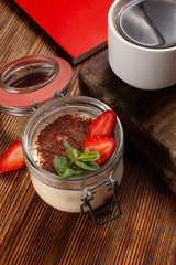 Traditional italian dessert tiramisu with mascarpone and cocoa with black coffee served on a dark wooden table with a book