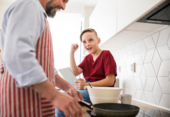Mature father with small son indoors in kitchen, making pancakes.