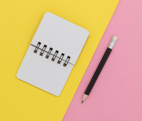 Open notebook and pencil on a yellow and pink diagonal background