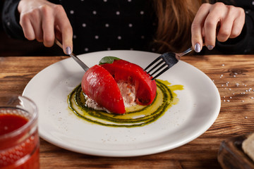 Woman is eating Bull's Heart tomato, stuffed with tuna and cheese, flavoured with fresh pesto sauce and basil on a white plate
