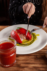 Woman is eating Bull's Heart tomato, stuffed with tuna and cheese, flavoured with fresh pesto sauce and basil on a white plate