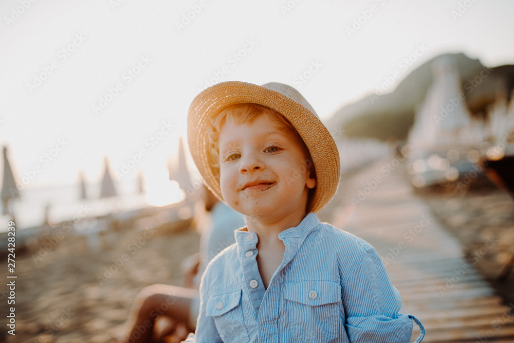 Sticker a small toddler boy standing on beach on summer holiday at sunset.