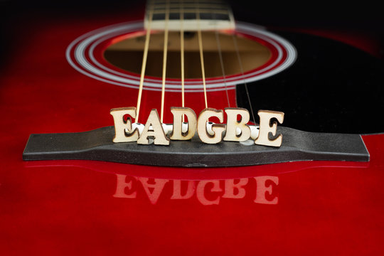 Musical notes EADGBE in corresponding to strings arrangement, with wooden letters, on the bridge of an acoustic guitar. Guitars bridge perspective. Creative background.