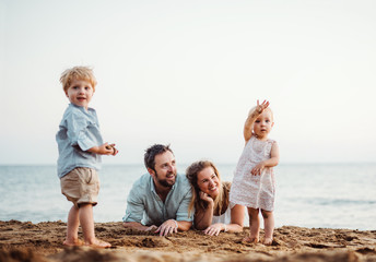 A family with two toddler children lying on sand beach on summer holiday.