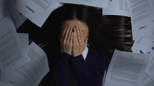 Scared woman covering face, looking at pile of documents, afraid to start work