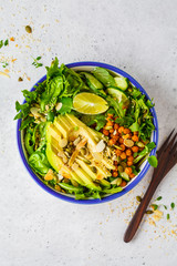 Green healthy salad with avocado, baked chickpeas and seeds in white bowl, top view.