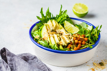 Green healthy salad with avocado, baked chickpeas and seeds in white bowl.