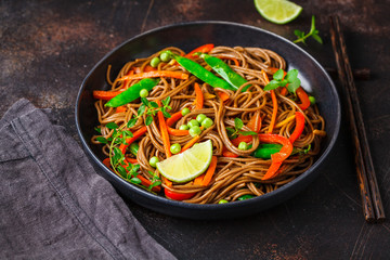 Vegan buckwheat soba noodles with vegetables in black plate on dark background.