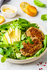 Green salad with avocado, cucumber and lentil cutlet in white plate.
