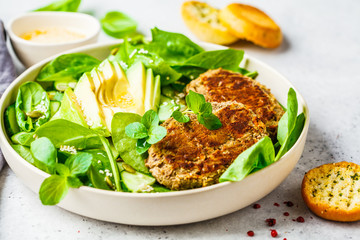 Green salad with avocado, cucumber and lentil patties in white plate.