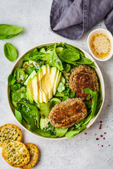 Green salad with avocado, cucumber and lentil patties in white plate.