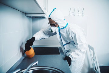 Exterminator in work wear spraying pesticide with sprayer. Selective focus.