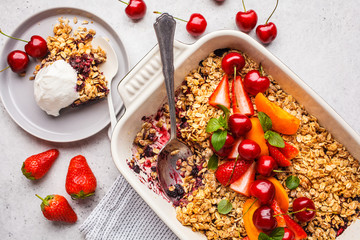 Fruits and berries oat crumble in oven dish on gray background, top view.