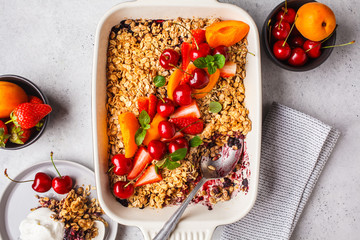 Fruits and berries oat crumble in oven dish on gray background, top view.