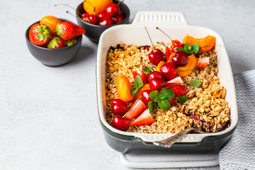 Fruits and berries oat crumble in oven dish on gray background.