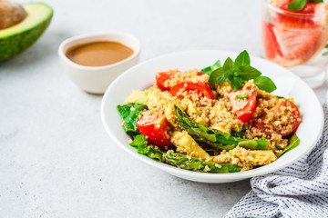 Green salad with quinoa, avocado and asparagus in a white bowl.