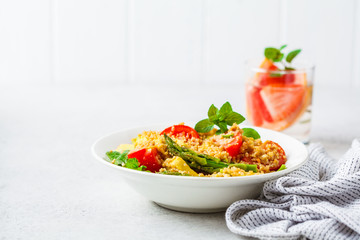 Green salad with quinoa, avocado and asparagus in a white bowl.