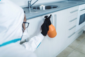 Exterminator in work wear spraying pesticide with sprayer. Selective focus.