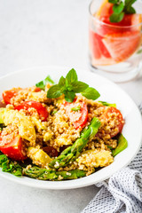 Green salad with quinoa, avocado and asparagus in a white bowl.