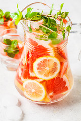 Grapefruit lemonade with lemon and mint in glass jug.